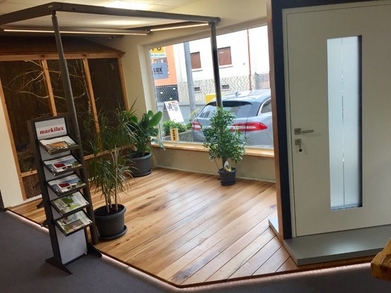 Moderner Showroom mit Haustür, Prospektständer, Holzboden und großen Fenstern.