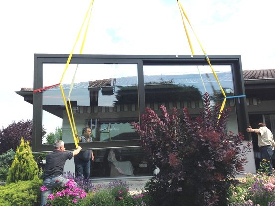Großes Fenster wird von mehreren Handwerkern mithilfe eines Krans in ein Haus eingesetzt.